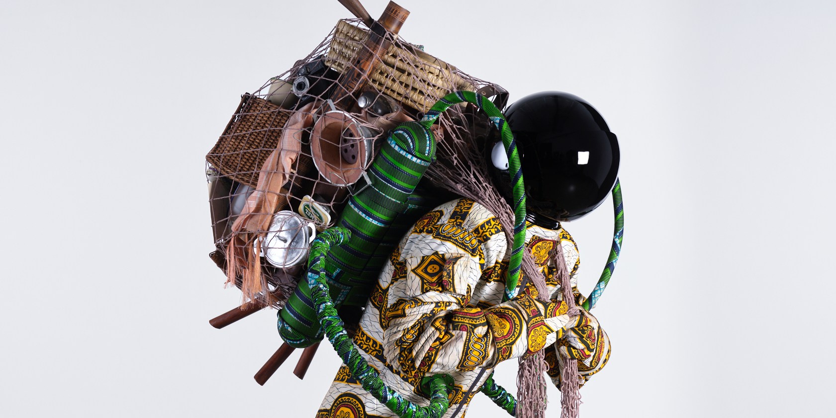A sculpture by Yinka Shonibare of a life-sized figure in an astronaut suit made of Dutch wax print fabric. The figure is carrying a large sack over their shoulder full of survival gear.