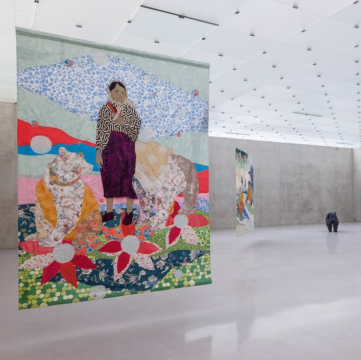 View of Malgorzata Mirga Tas's exhibition, with colorful tapestries hanging from the ceiling and sculptures of bears.